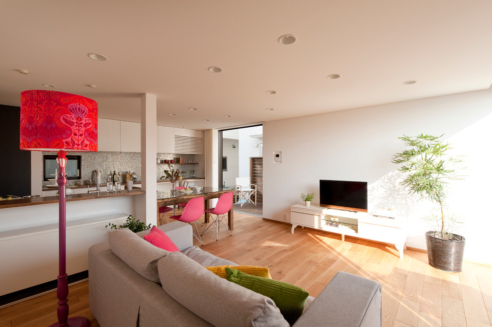 Пример оригинального дизайна: открытая гостиная комната в стиле модернизм с белыми стенами, светлым паркетным полом, отдельно стоящим телевизором и коричневым полом
