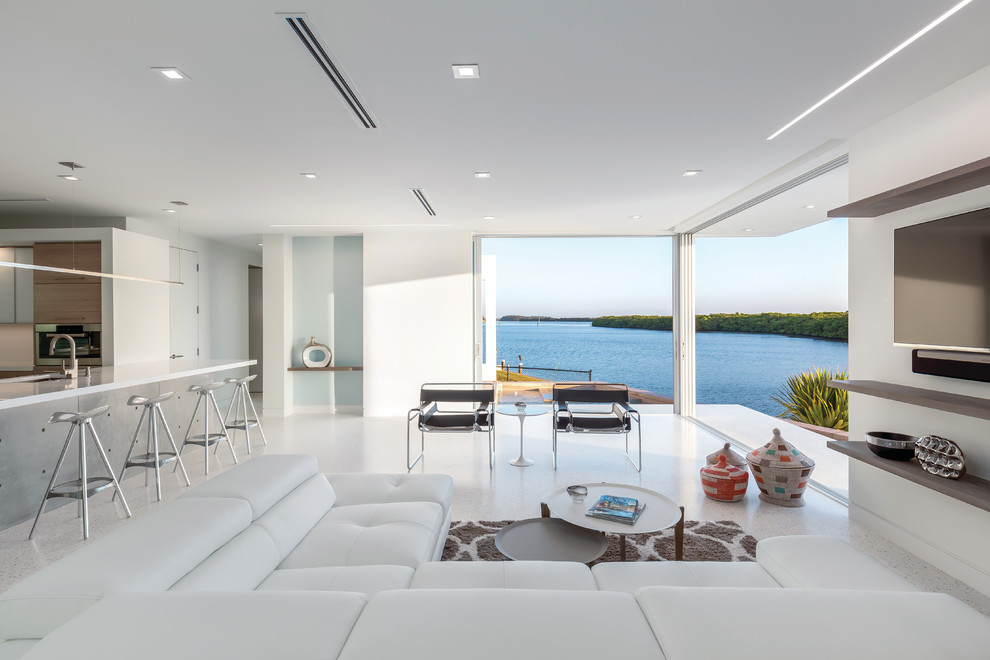 Идея дизайна: большая открытая гостиная комната в стиле модернизм с белыми стенами, бетонным полом, телевизором на стене и белым полом