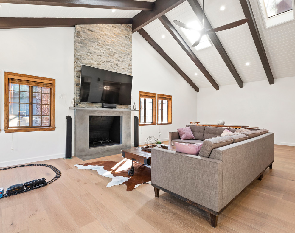 This is an example of a large traditional open plan living room in Los Angeles with grey walls, light hardwood flooring, a standard fireplace, a stone fireplace surround, a built-in media unit and beige floors.
