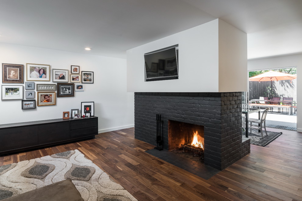 Photo of a medium sized contemporary formal open plan living room in Portland with white walls, dark hardwood flooring, a two-sided fireplace, a brick fireplace surround, a wall mounted tv and brown floors.