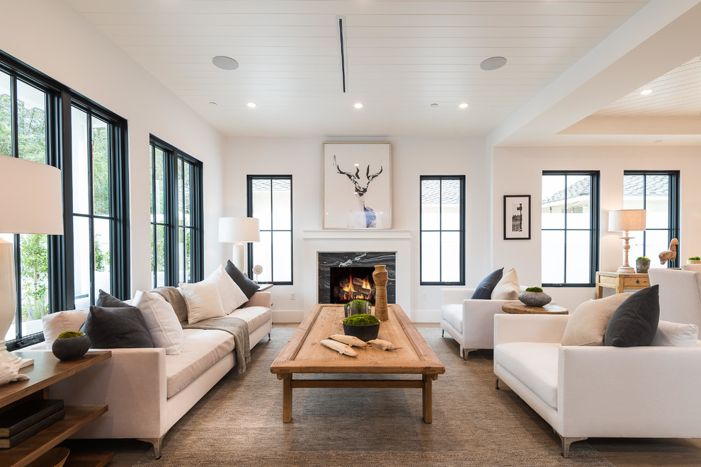 Repräsentatives, Fernseherloses Landhausstil Wohnzimmer mit weißer Wandfarbe, braunem Holzboden, Kamin, Kaminumrandung aus Stein und braunem Boden in Los Angeles