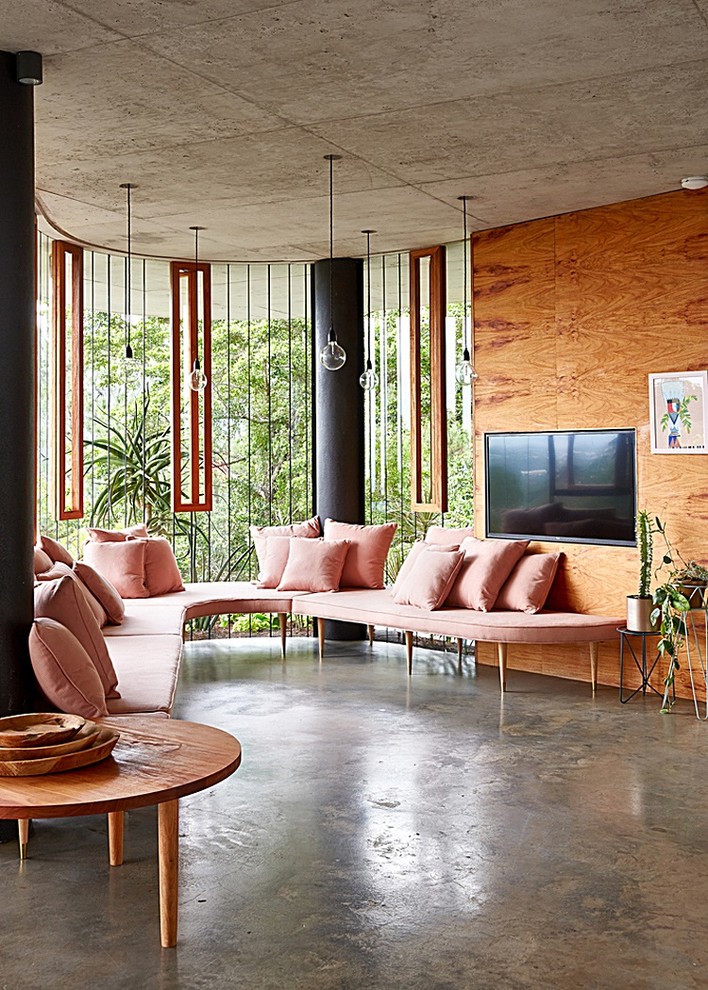 Imagen de salón tropical con paredes marrones, suelo de cemento y televisor colgado en la pared