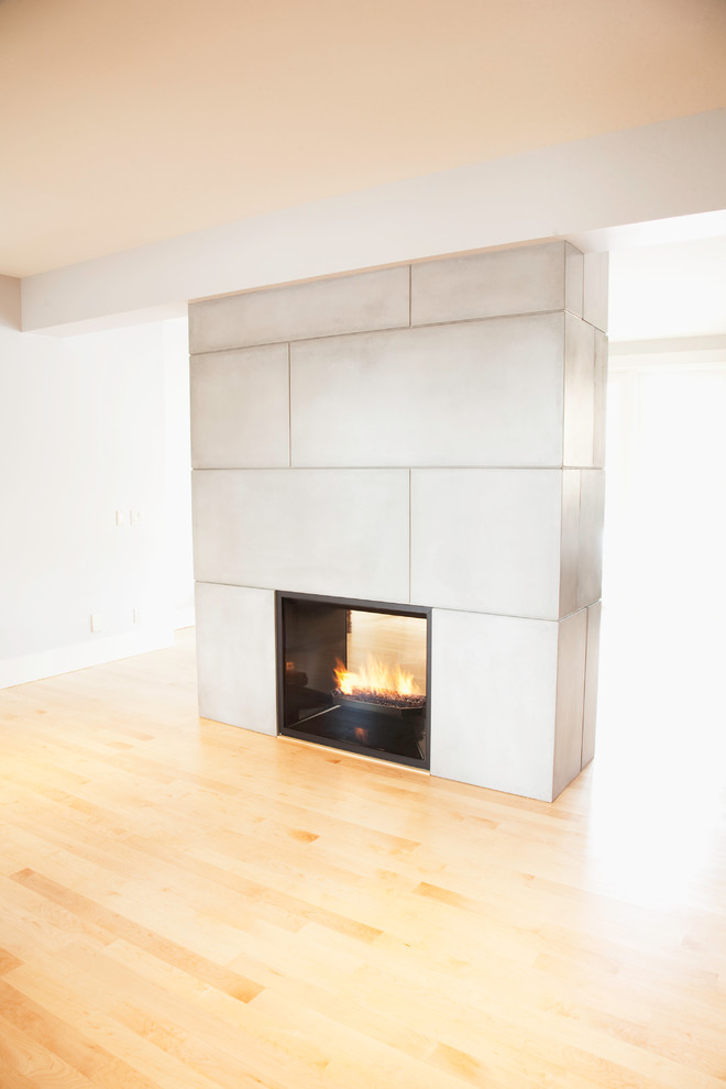 Fernseherloses, Offenes Modernes Wohnzimmer mit Kaminumrandung aus Beton, hellem Holzboden und Tunnelkamin in Calgary