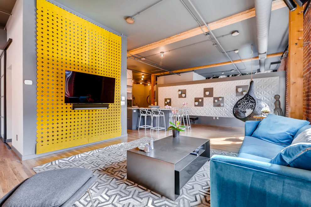 Пример оригинального дизайна: открытая гостиная комната в стиле лофт с серыми стенами, светлым паркетным полом, телевизором на стене и коричневым полом
