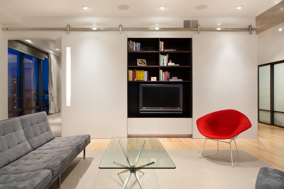 Inredning av ett minimalistiskt allrum med öppen planlösning, med vita väggar, ljust trägolv och en väggmonterad TV