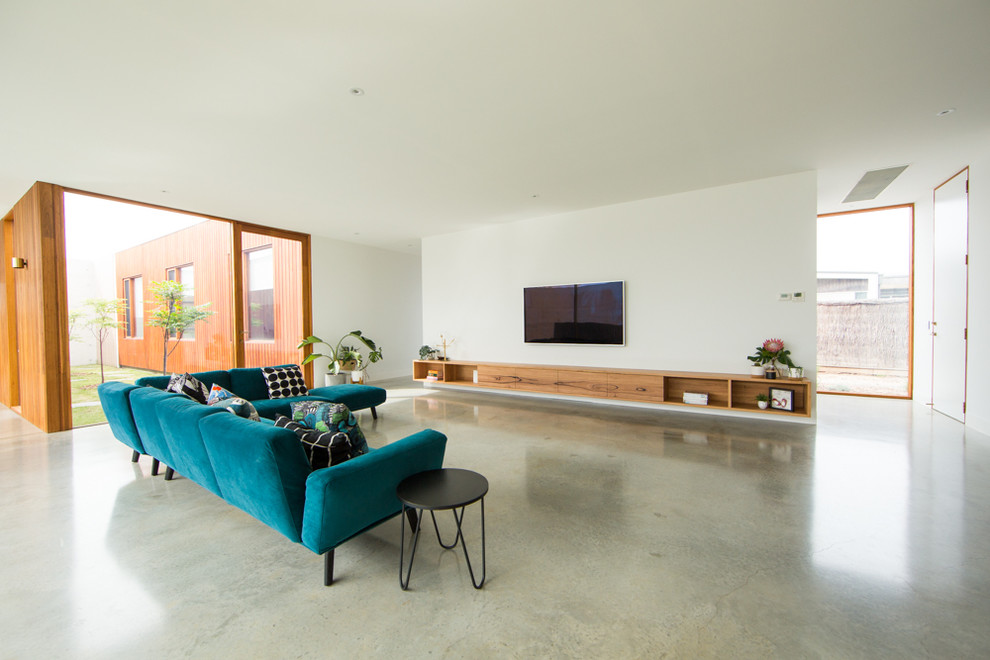 Пример оригинального дизайна: огромная парадная, открытая гостиная комната в современном стиле с белыми стенами, бетонным полом, телевизором на стене и серым полом