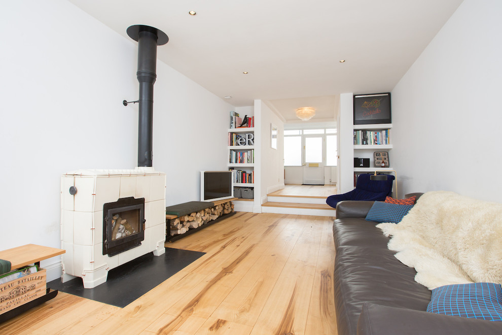 Cette image montre un salon minimaliste de taille moyenne et ouvert avec parquet clair, un poêle à bois, un mur blanc, un téléviseur indépendant, un sol beige et un manteau de cheminée en métal.