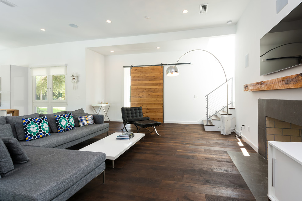 На фото: гостиная комната в современном стиле с белыми стенами, темным паркетным полом, стандартным камином и телевизором на стене с