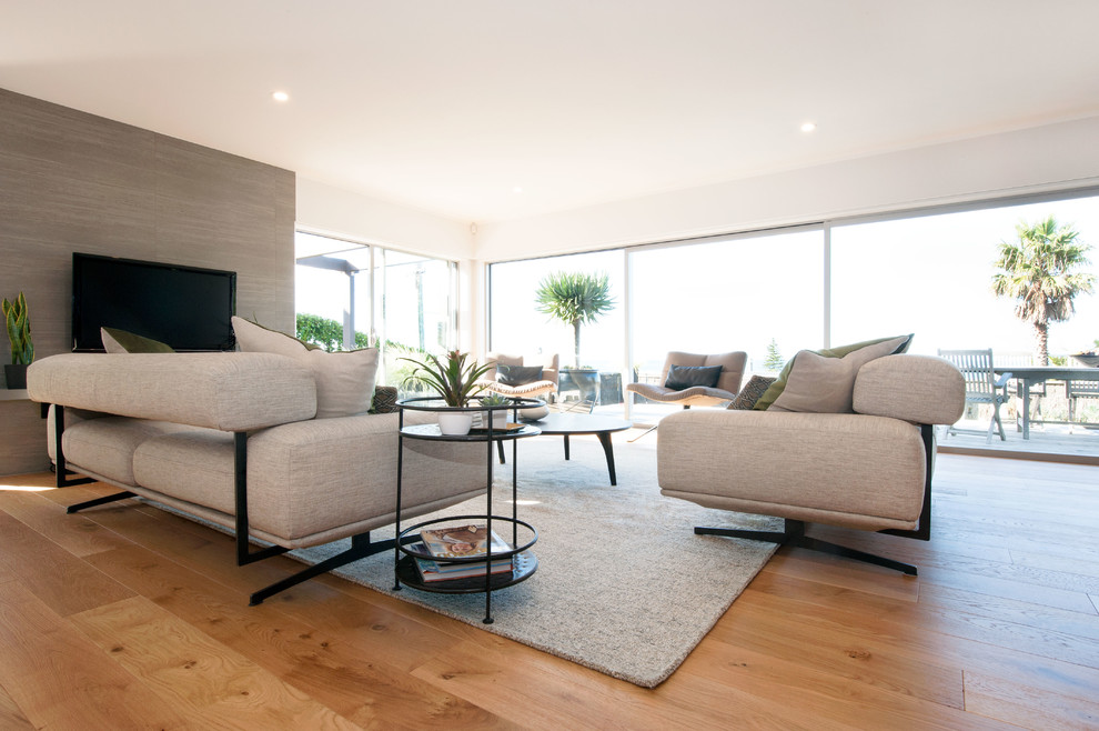 This is an example of a medium sized contemporary formal open plan living room in Auckland with grey walls, medium hardwood flooring, no fireplace, a wall mounted tv and beige floors.
