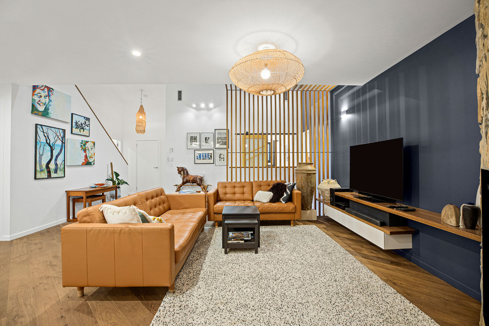 Geräumiges, Offenes Modernes Wohnzimmer mit braunem Holzboden, Eckkamin, Kaminumrandung aus Stein, TV-Wand, grauer Wandfarbe und braunem Boden in Sonstige