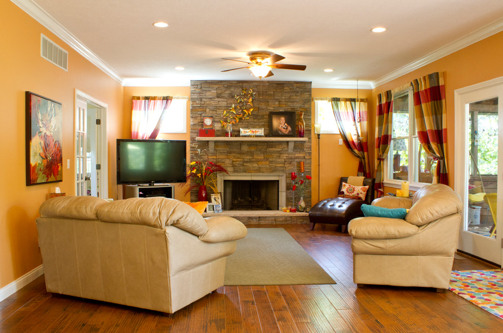 Foto di un soggiorno classico aperto con pareti arancioni, pavimento in legno massello medio, camino classico e cornice del camino in pietra