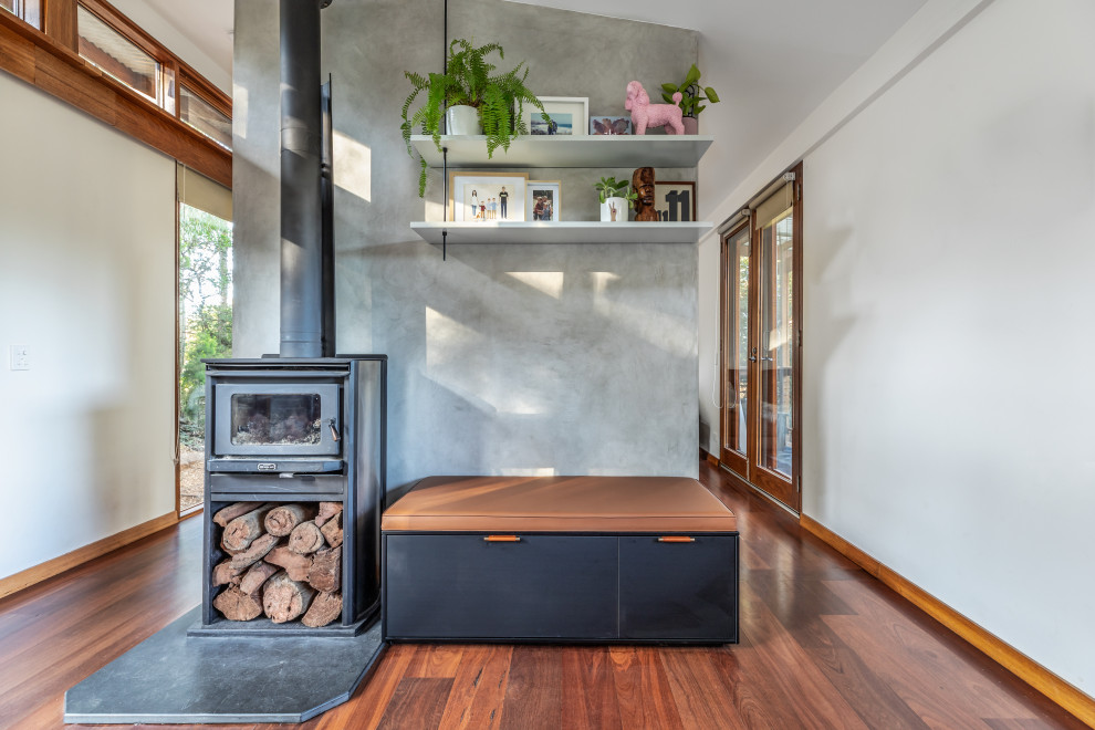 Mittelgroßes, Offenes Modernes Wohnzimmer mit grauer Wandfarbe, braunem Holzboden, Kamin, Kaminumrandung aus Beton, braunem Boden und vertäfelten Wänden in Adelaide