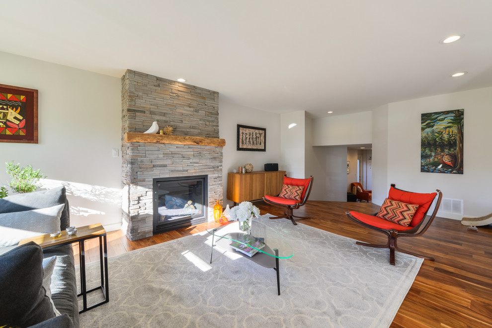 Mittelgroßes, Repräsentatives, Fernseherloses, Offenes Modernes Wohnzimmer mit weißer Wandfarbe, braunem Holzboden, Kamin, Kaminumrandung aus Stein und braunem Boden in Calgary