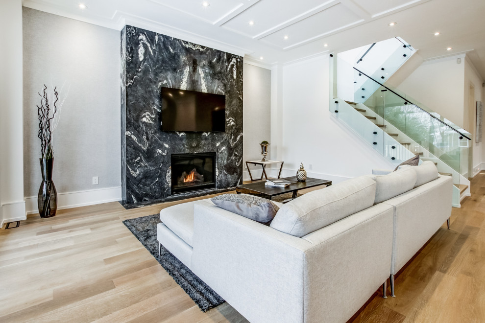 Large contemporary open plan living room in Toronto with grey walls, medium hardwood flooring, a standard fireplace, a stone fireplace surround, a wall mounted tv and brown floors.