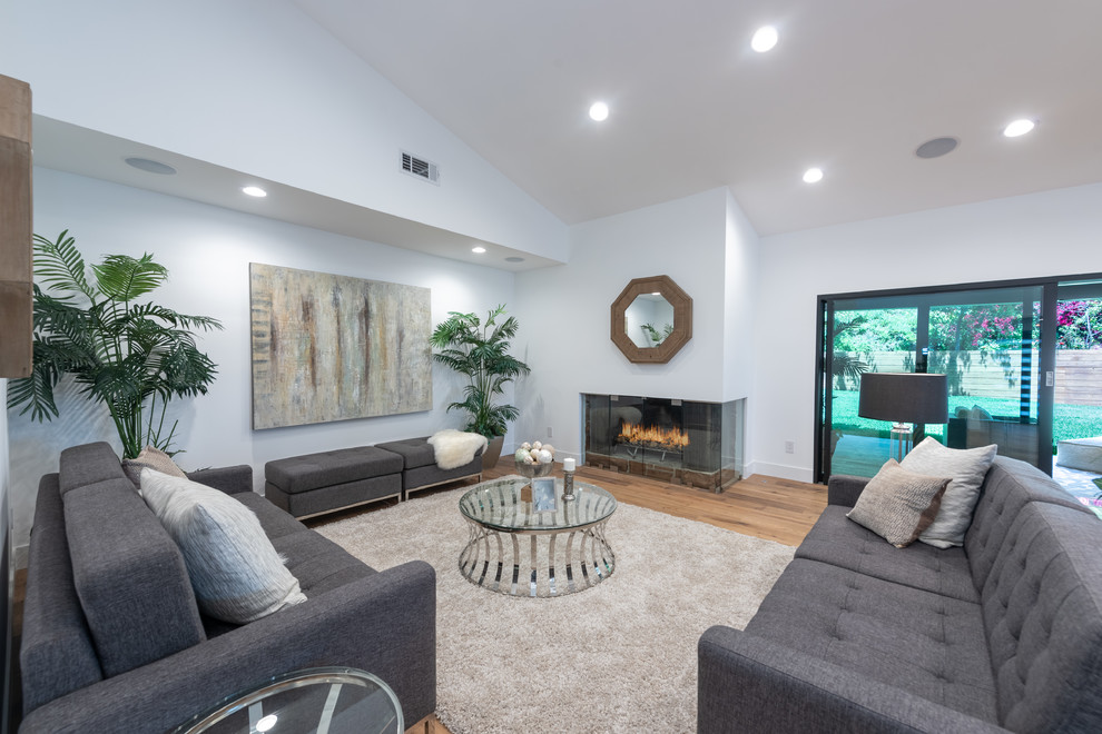 ロサンゼルスにあるラグジュアリーな広いコンテンポラリースタイルのおしゃれなリビング (白い壁、淡色無垢フローリング、コーナー設置型暖炉、壁掛け型テレビ、茶色い床) の写真