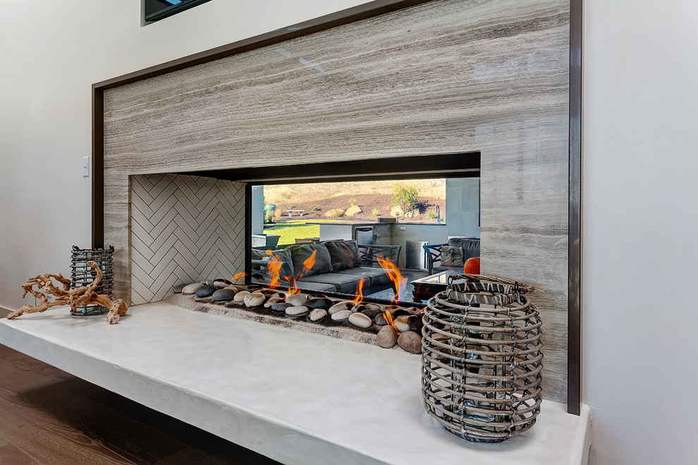 Foto di un soggiorno design con pareti grigie, pavimento in legno massello medio, camino bifacciale e cornice del camino in pietra