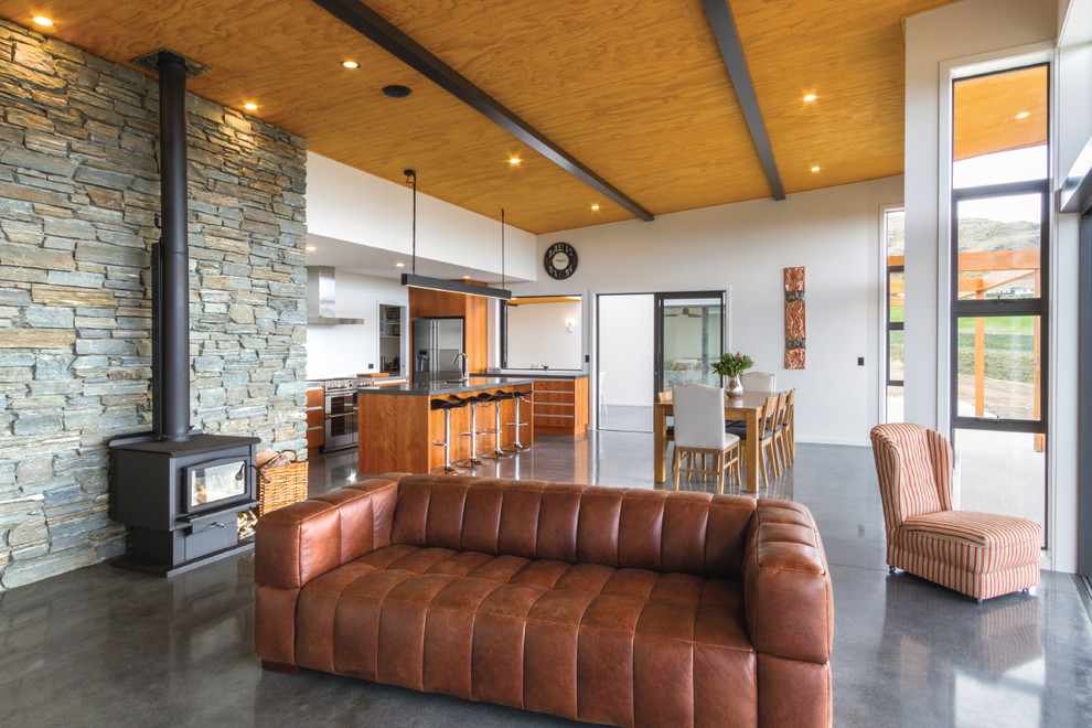 Offenes Modernes Wohnzimmer mit weißer Wandfarbe, Betonboden und Kaminofen in Dunedin