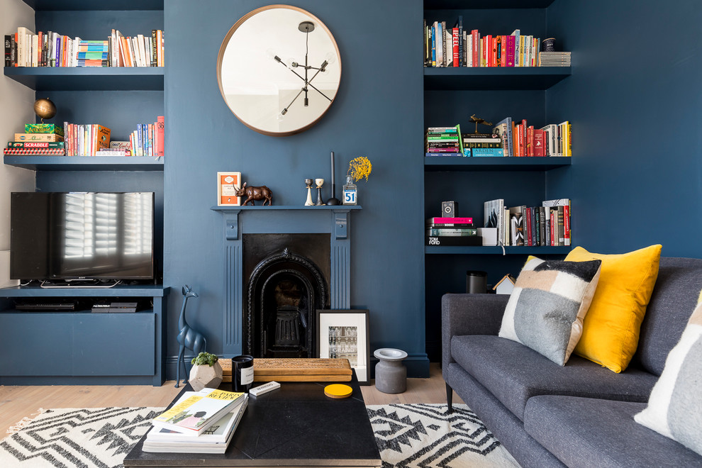 Mittelgroße, Abgetrennte Moderne Bibliothek mit blauer Wandfarbe, hellem Holzboden, Kaminumrandung aus Holz, Kamin, freistehendem TV und beigem Boden in London