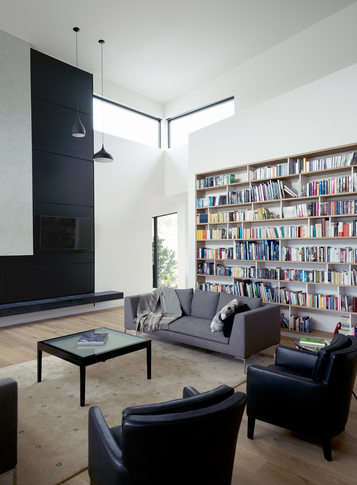 Modelo de biblioteca en casa abierta contemporánea con paredes blancas, suelo de madera en tonos medios, televisor colgado en la pared y suelo marrón