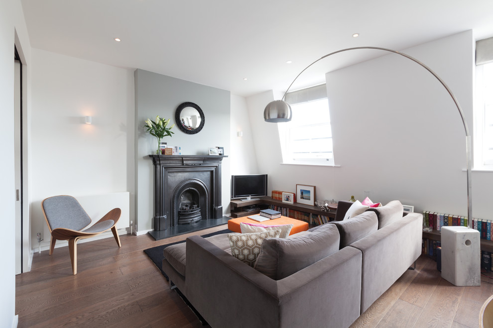 Trendy formal and enclosed medium tone wood floor living room photo in London with white walls, a standard fireplace and a tv stand