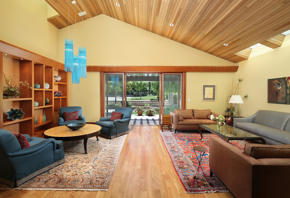 Imagen de salón para visitas abierto actual sin chimenea y televisor con paredes amarillas y suelo de madera en tonos medios