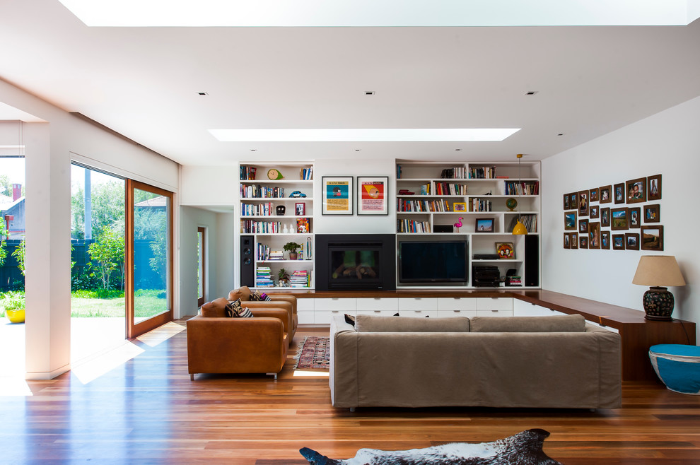 Ispirazione per un soggiorno design aperto con pareti bianche, pavimento in legno massello medio e TV a parete