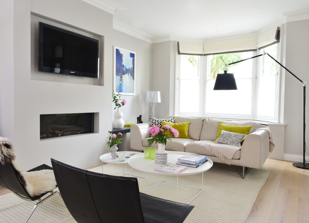 Example of a trendy open concept light wood floor living room design in London with gray walls, a ribbon fireplace, a wall-mounted tv and a plaster fireplace