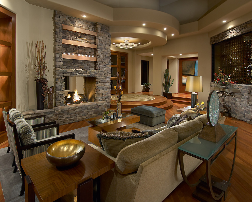 Exemple d'un salon tendance ouvert avec une salle de réception, un mur beige, un sol en bois brun, une cheminée double-face et un manteau de cheminée en pierre.