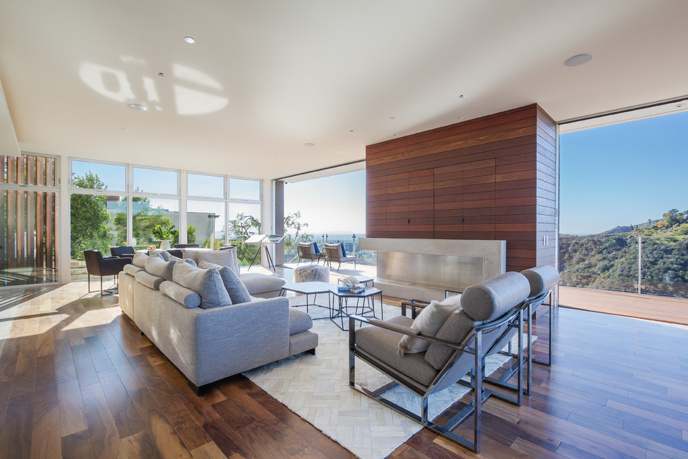 Offenes Modernes Wohnzimmer mit braunem Holzboden, Gaskamin, Kaminumrandung aus Beton und verstecktem TV in Los Angeles