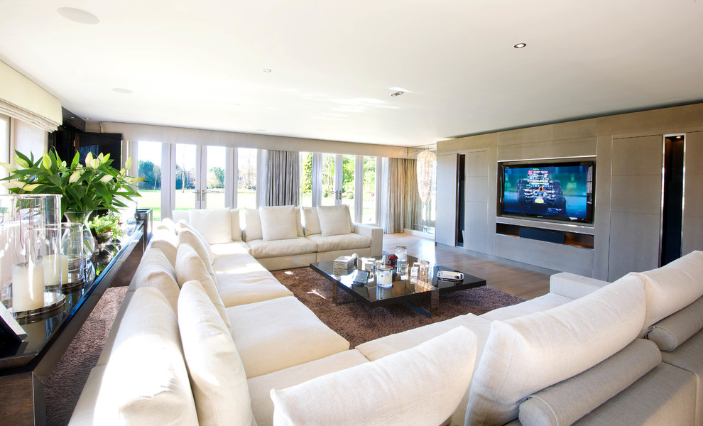 Modern inredning av ett stort vardagsrum, med beige väggar, mellanmörkt trägolv och en väggmonterad TV