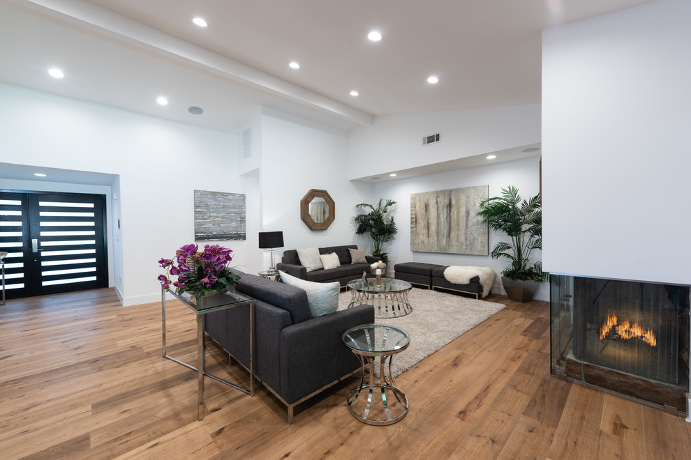 Immagine di un grande soggiorno design aperto con sala formale, pareti bianche, parquet chiaro, camino ad angolo, TV a parete e pavimento marrone
