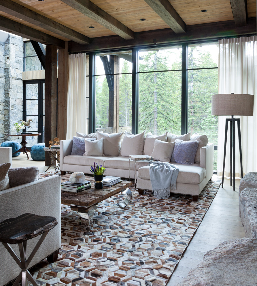 Exemple d'un salon montagne ouvert avec parquet clair, une cheminée standard, un manteau de cheminée en pierre, un sol beige et poutres apparentes.