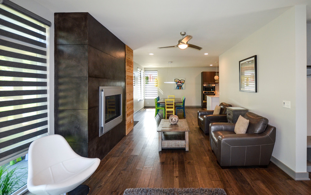 Cette image montre un salon design de taille moyenne et ouvert avec une salle de réception, un mur gris, un sol en bois brun, une cheminée standard, un manteau de cheminée en béton et un sol marron.