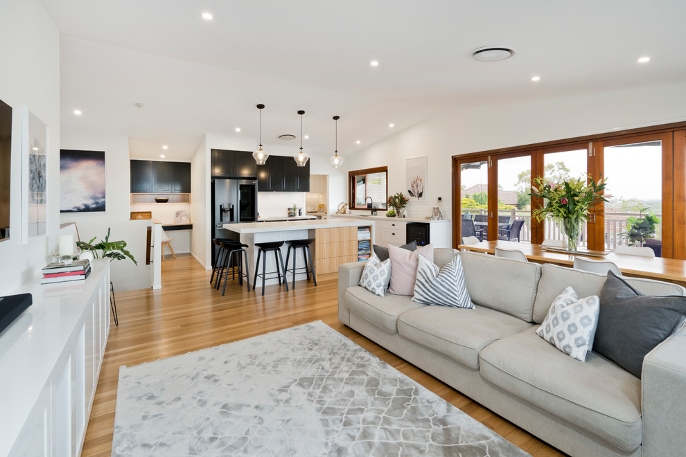 Example of a large trendy open concept light wood floor and beige floor living room design in Brisbane with white walls and a wall-mounted tv