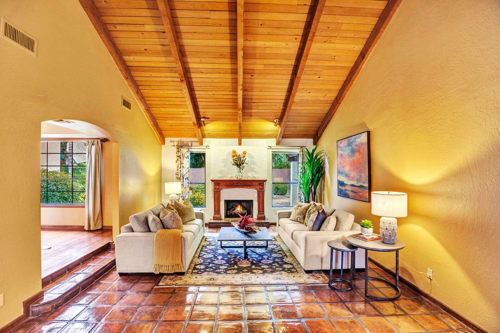 フェニックスにある高級な中くらいなサンタフェスタイルのおしゃれな応接間 (黄色い壁、テラコッタタイルの床、標準型暖炉、漆喰の暖炉まわり、マルチカラーの床) の写真
