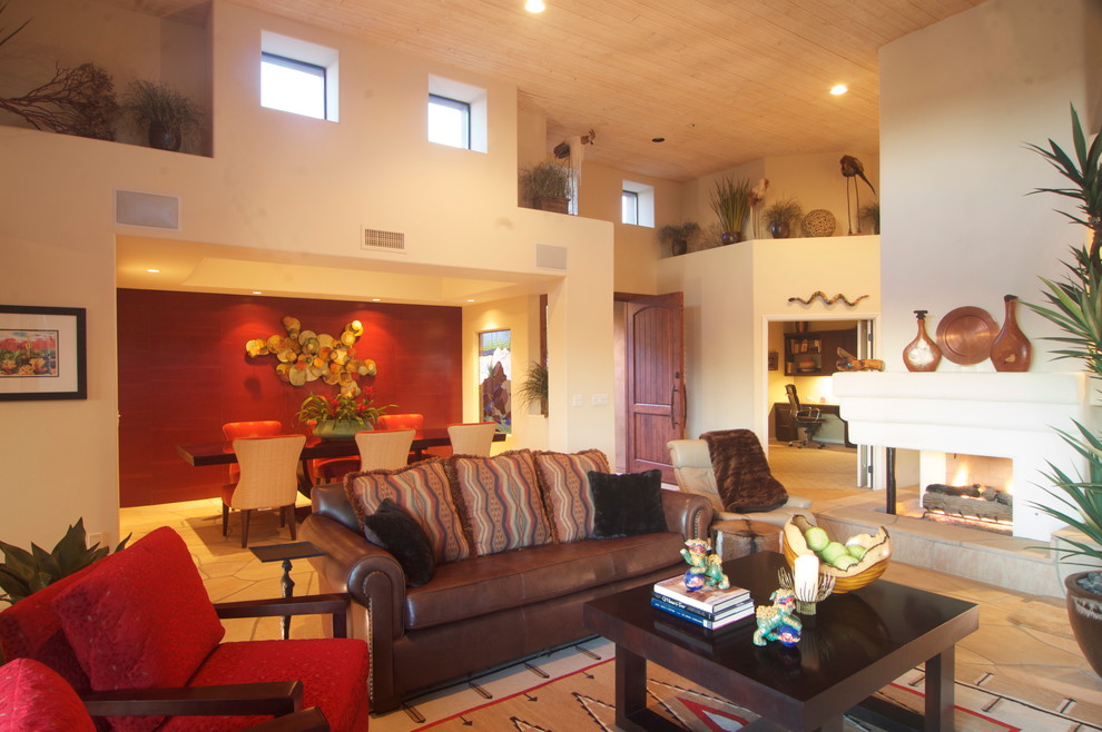 Cette photo montre un grand salon sud-ouest américain ouvert avec une cheminée double-face, une salle de réception, un mur beige, un manteau de cheminée en plâtre, aucun téléviseur et un sol marron.