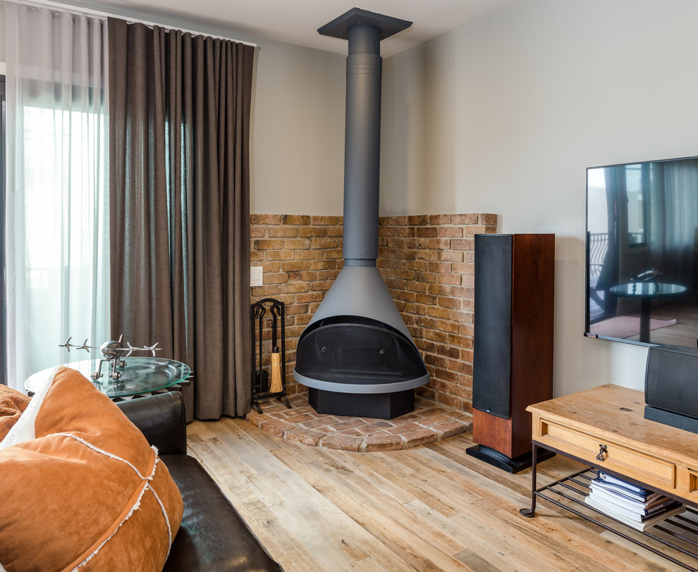 Inspiration pour un salon traditionnel de taille moyenne et ouvert avec un mur gris, un sol en bois brun, un poêle à bois, un manteau de cheminée en brique et un téléviseur fixé au mur.