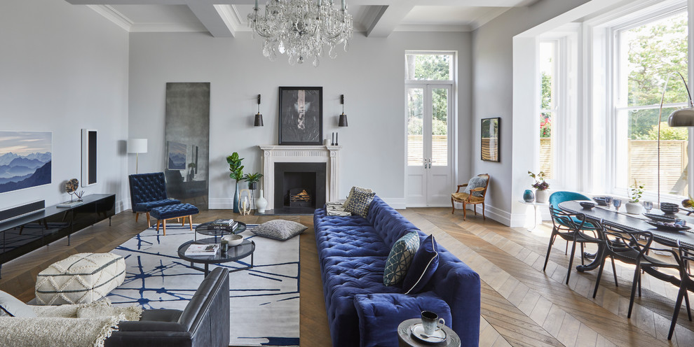 Large classic open plan living room in Hertfordshire with grey walls, a standard fireplace, a plastered fireplace surround, a wall mounted tv, medium hardwood flooring and feature lighting.