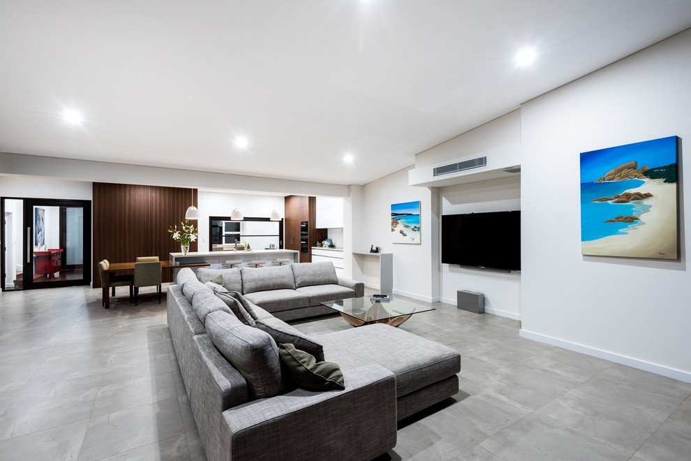 На фото: огромная открытая гостиная комната в стиле модернизм с телевизором на стене, белыми стенами, полом из керамогранита и серым полом с