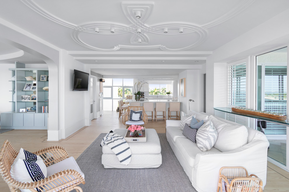 This is an example of a nautical living room in Miami with white walls, light hardwood flooring, a wall mounted tv and beige floors.