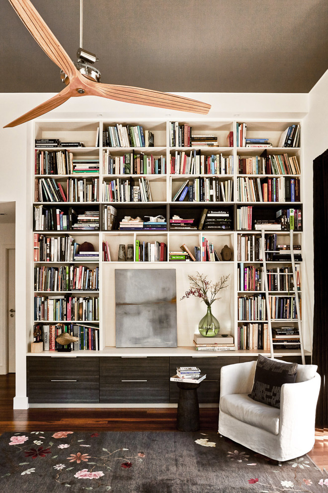 Foto på ett funkis allrum med öppen planlösning, med ett bibliotek, vita väggar och mörkt trägolv