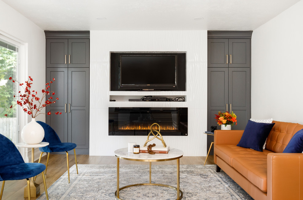 На фото: открытая гостиная комната среднего размера в современном стиле с белыми стенами, полом из ламината, стандартным камином, фасадом камина из плитки, телевизором на стене, бежевым полом и коричневым диваном