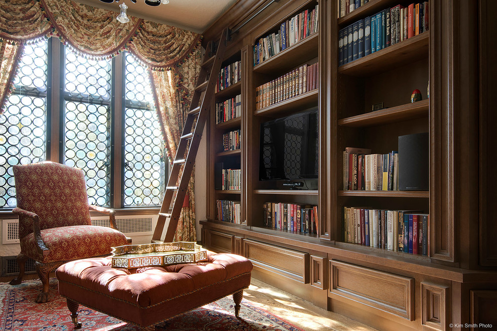 Modelo de biblioteca en casa cerrada clásica pequeña sin chimenea con paredes beige, suelo de madera en tonos medios y televisor independiente