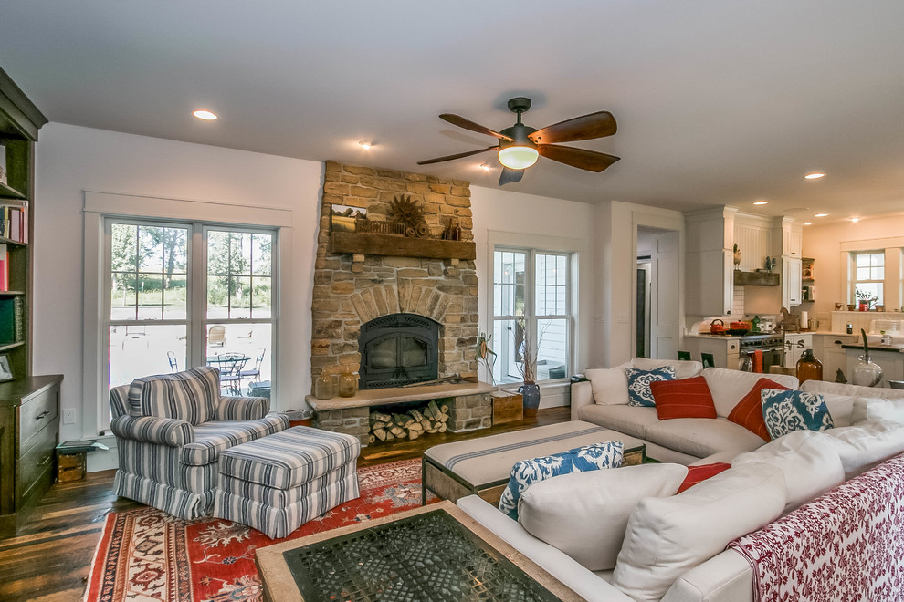 Inspiration for a country open plan living room in Cedar Rapids with white walls, dark hardwood flooring, a standard fireplace, a stone fireplace surround and brown floors.