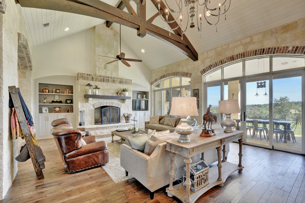 This is an example of a country open plan living room in Austin with white walls, dark hardwood flooring, a standard fireplace, a stone fireplace surround, a freestanding tv and feature lighting.