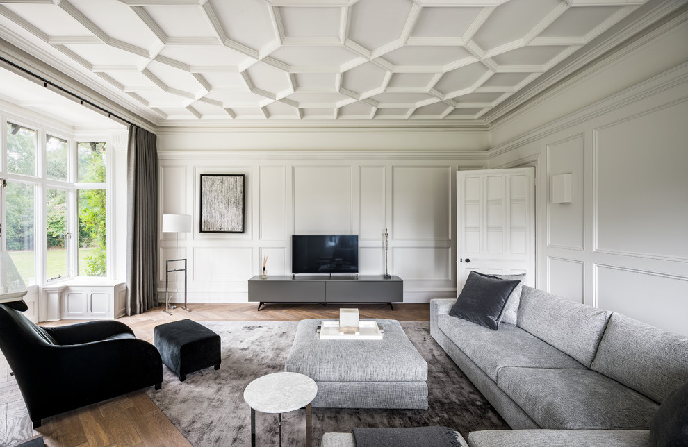 На фото: большая изолированная гостиная комната в стиле неоклассика (современная классика) с серыми стенами, светлым паркетным полом, отдельно стоящим телевизором, коричневым полом и эркером с