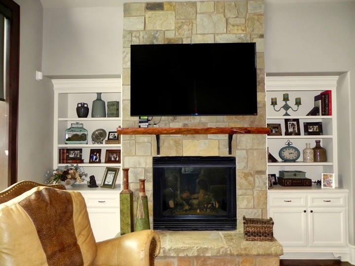 ヒューストンにある広いラスティックスタイルのおしゃれなLDK (ベージュの壁、コンクリートの床、標準型暖炉、石材の暖炉まわり、壁掛け型テレビ) の写真