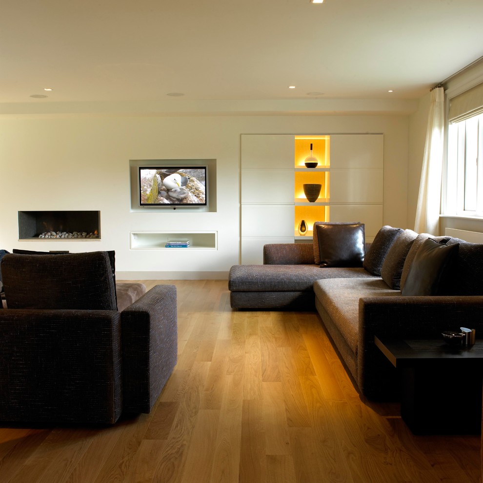 Immagine di un grande soggiorno chiuso con pareti bianche, parquet chiaro e TV a parete