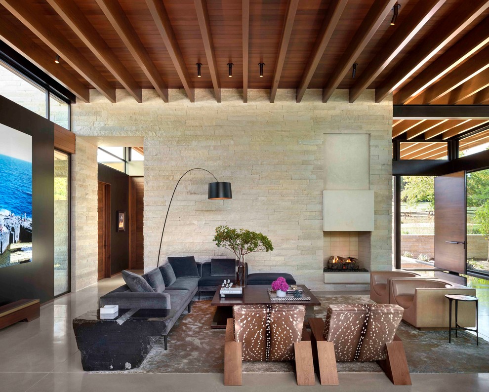 Cette photo montre un salon tendance ouvert avec sol en béton ciré, une cheminée standard, un manteau de cheminée en pierre, un sol gris et un mur en pierre.