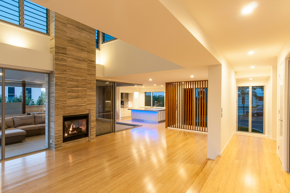 Стильный дизайн: большая открытая гостиная комната в современном стиле с белыми стенами, полом из бамбука, двусторонним камином и фасадом камина из плитки без телевизора - последний тренд